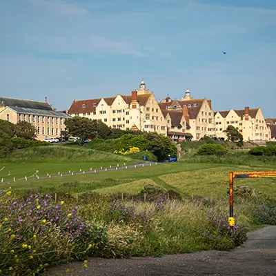 A scenic view of a large educational building surrounded by green fields and flowers, under a clear blue sky.